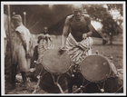 1 Male in Striped Body Cloth Playing 2 Drums With 2 Onlookers