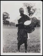 1 male dressed in tunic and body cloth carrying a small drum