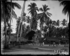 Group of children sitting near house with a large wooden platform porch underneath large coconut palms