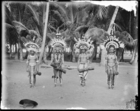 Four young men wearing jewellery and elaborate feather headdresses (clan badges), standing holding drums (see also RAI No. 33440-6) Dauncey's hat in foreground ?