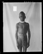 Young boy with shaved head and tight perineal woven band, standing against white cloth backdrop (see also RAI No. 34269)