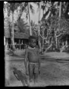 young boy wearing tooth necklace, standing in front of house
