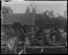 Four boys sitting on a canoe, each holding a pet (?) cuscus or wallaby (?)