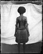 back view of woman, tattooed from head to foot, standing against white cloth backdrop (see also RAI No. 34383 ?)