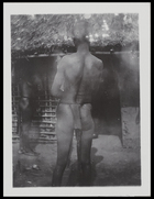 woman with cicatrices standing with her back to the camera, entrance to hut in background