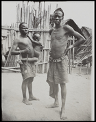 two men, one carrying child, in front of wooden stockade