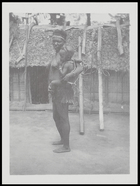 woman holding child standing outside thatched hut