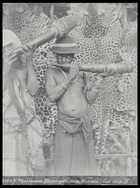 two men, one wearing a European hat ?, blowing large horn trumpets, standing in front of leopard skins stretched over a wooden framework