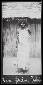 woman wearing striped cloth dress, standing outside a hut