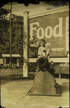 Photograph of a boy sitting on a cannon in front of a 'Food will win the war' billboard, Memphis, TN