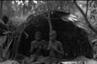 Two women sat outside the entrance to a dome-shaped shelter and another woman or man standing just to the side.