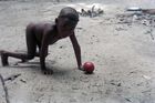 Close-up of a child crouching on all fours with a round red fruit on the ground just in front of him or her.