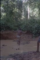 A youth wearing shorts jumping into a muddy river or water hole in the forest.