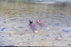 Two children swimming in the shallow and clear waters of a river.