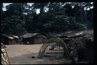 The buildings and shelters in a settlement at the edge of a clearing in the forest.