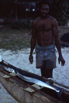 1993.6.2.1680: (Process date July 78) Freddie standing behind Nuwar lying on canoe on shore, taken from top